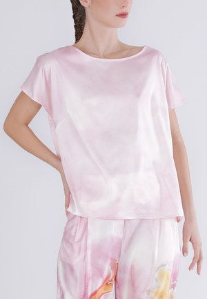 Kobieta prezentująca jasnoróżową, satynową bluzkę z krótkim rękawem o luźnym kroju oraz pasujące spodnie z abstrakcyjnymi wzorami w odcieniach różu i pomarańczy.