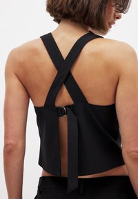 Črn skrajšan top z prečnimi pasovi na hrbtu, detajlom z zaponko ter gladko, mat teksturo in odprtim zadnjim delom.