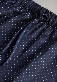 Granatowa tkanina o błyszczącej fakturze, zdobiona białymi kropkami i elastycznym pasem z wiązaną kokardą.