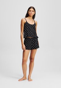 Conjunto de pijama negro que incluye una camiseta sin mangas de patrón con un dobladillo con volantes y pantalones cortos a juego con banda elástica en la cintura y bordes en forma de concha.