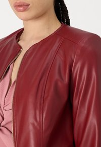 Giacca in pelle rossa con chiusura a zip, caratterizzata da una texture liscia e un design aderente. Lo stile senza colletto offre una silhouette pulita.