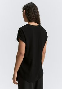 Schwarzes T-Shirt mit umgeschlagenen kurzen Ärmeln, runden Halsausschnitt und abgerundetem Saum. Hergestellt aus einem glatten, leichten Stoff. Rückansicht gezeigt.