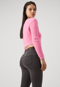 Pink fuzzy cropped sweater with long sleeves paired with fitted dark gray denim jeans featuring back pockets and a waistband.