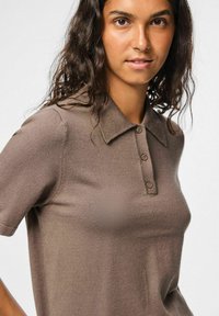 Brun stickad polo-shirt med en mjuk textur, med krage, korta ärmar och tre-knäppning.