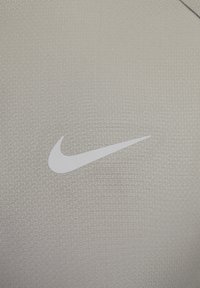 Tejido atlético gris claro con un patrón texturizado, que presenta un prominente logo de Nike en blanco.