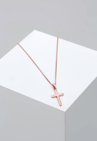 Roosakullast risti ripats õhukesel ketil, millel on sile, poleeritud pind ja lihtne geomeetriline kujundus. Kuvatud valgel postamendil.