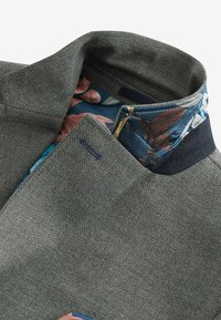 Grau strukturiertes Stoffjackett mit einem kontrastierenden floralem Innenkragen in Blau-, Pink- und Grüntönen. Auffälliges akzentuiertes Detail in Marineblau.