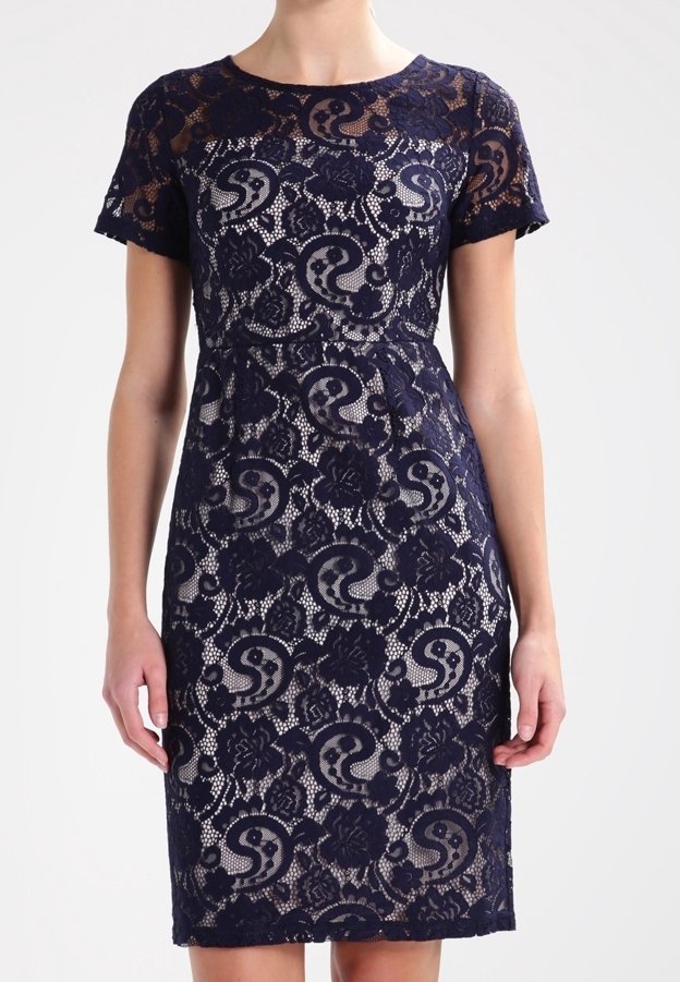 Femme portant une robe en dentelle bleu marine à manches courtes avec des motifs floraux paisley sur une doublure beige.