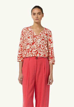Red and white floral patterned blouse with a V-neckline and three-quarter sleeves, paired with high-waisted pink trousers. Smooth fabric texture.