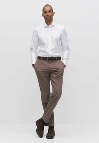 Witte langmouwen shirt gecombineerd met bruine gestructureerde broeken en donkerbruine laarzen, met een gladde afwerking en een klassieke riem.
