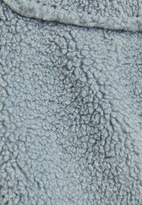 Light blue, textured fleece fabric with a soft, fluffy surface and a slightly raised, uneven pattern throughout.