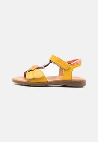 Gelbe Ledersandalen mit floraler Akzentuierung, offenes Design und verstellbarem Riemen; natürliche, braune Sohle mit glatter Textur.