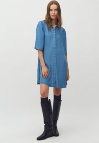 Denim obleka z gumbnim zapiranjem, kratkimi naborkami na rokavih in sproščenim krojem. Ima dolžino do kolen in rahlo obrabljene robove.