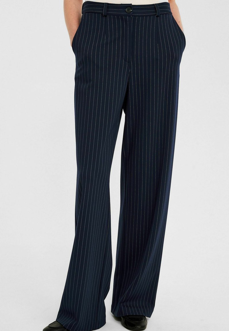 Marineblauwe gestreepte brede broek met een gladde textuur, voorzien van voorzakken en een knoopsluiting bij de tailleband, gecombineerd met zwarte schoenen.