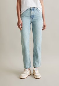 Lichtblauwe denim jeans met een rechte snit, hoge taille, subtiele vervaging en een klassieke vijf-pocketontwerp, gecombineerd met witte sneakers.