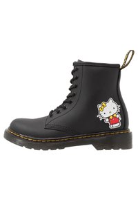 Černé šněrovací boty s tlustou podrážkou a žlutým prošíváním, s dekorací postavy Hello Kitty na vnější straně poblíž paty.