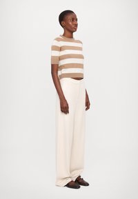 Short-sleeve striped sweater in beige and white; high-waisted cream pants; brown flat shoes; smooth texture and relaxed fit.