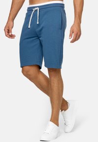 Blauwe jersey shorts met witte trekkoord en elastische tailleband, met zijzakken en een relaxed fit, gedragen met witte sneakers.