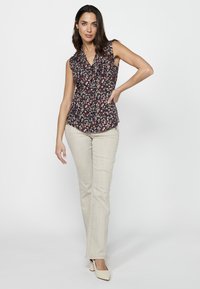 Top senza maniche floreale in blu navy con motivi rossi e bianchi, abbinato a pantaloni fitted beige chiaro e scarpe con tacco color crema. Tessuto liscio.