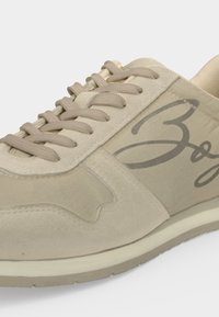 Baskets beiges à lacets avec panneaux en daim et tissu, semelle épaisse et logo en cursive sur le côté.