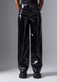 Calças largas de vinil preto brilhante com uma cintura alta, apresentando um botão frontal, dois bolsos laterais e um acabamento suave e brilhante.