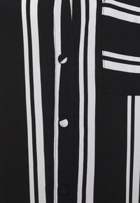 Czarna i biała koszula w paski z zapięciem na guziki, teksturą materiału oraz kieszenią na piersi z poziomymi paskami.