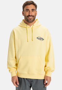 Yellow hoodie with a front pocket and drawstrings. Features a logo in gray and pink on the left chest. Made of soft fabric.