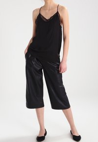 Svart linne med spetsdetaljer, kombinerat med svarta faux läder culottes med avslappnad passform och ankellång klippning. Svarta platta skor fullbordar looken.