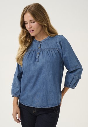 Denim bluza z okroglo oblikovano ovratnikom, tremi gumbi in nabranimi detajli. Ima napihnjene rokave z elastičnimi manšetami. Modra tkanina z mehko teksturo.