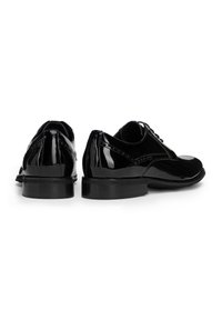 Zapatos de vestir de charol negro con un tacón bajo, que presentan un acabado suave, puntera redondeada y costuras decorativas a lo largo de los lados.