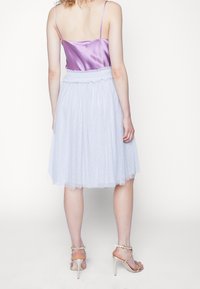 Lilac satin camisole dengan tali tipis, dipadukan dengan rok tulle biru muda yang dihiasi pola bintik-bintik. Model mengenakan sandal hak tinggi berwarna beige.