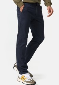 Chino bleu marine en tissu doux, avec une coupe classique, poches latérales et fermeture éclair. Associés à des baskets grises et jaunes.