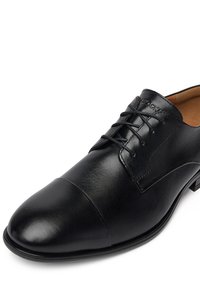 Must have musta nahast kleitkingad, millel on ümar nina, sile pind, nööbid ja diskreetne logo keelel.