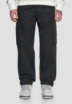 Pantalons cargo noirs avec poches latérales, fabriqués en tissu durable, présentant un design à jambe droite et des coutures visibles. Associés à des baskets grises.
