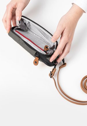 Black zippered wallet with a gray-lined interior, featuring a red accent pocket and brown leather strap. The wallet is held in two hands.