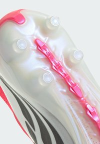 Κοντινή λήψη διαφανούς σόλας παπουτσιού με έξι καρφιά και μια ροζ δομή υποστήριξης "Power Spine" στο κέντρο.