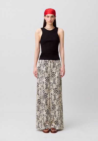 Top negro sin mangas combinado con pantalones de cintura alta y pierna ancha con fondo crema y estampado de leopardo negro, complementados con zuecos marrones.