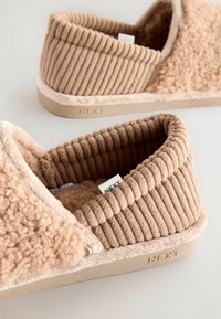 Chaussons marron clair avec dessus en tissu côtelé et doublure douce et moelleuse. La semelle est beige avec le mot "NEXT" en relief. Détails de surface texturée.
