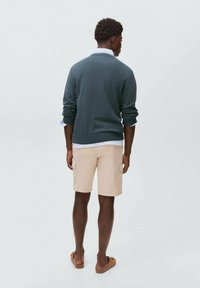 Dark green sweater, beige cargo shorts; fabric is smooth and lightweight. Model is wearing brown sandals; view is from behind.