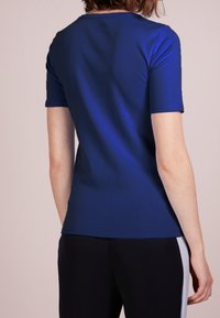 Top de manga corta azul marino con cuello redondo, textura suave y diseño ajustado, combinado con pantalones negros que presentan acentos laterales blancos.