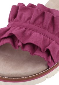Pink suede slide sandal featuring a ruffled upper design, soft interior, and textured sole with a contrasting white edge.