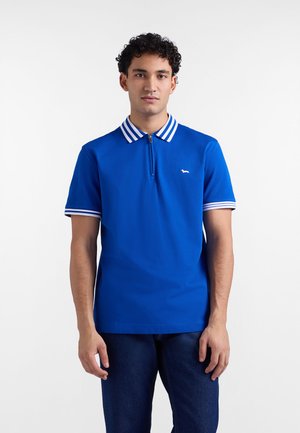 Plava polo majica s poluzipom, ukrašena prugastim ovratnikom i manžetama na rukavima. Suptilan logotip na lijevoj strani prsa. Glatka tekstura.