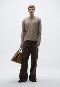 Hosszú ujjú bézs ing kis logóval, barna bőszárú nadrág, valamint texturált barna kézitáska cipzárokkal és dupla fogantyúval. Fekete cipők.