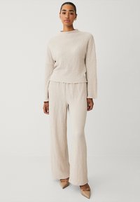 Beige textuur trui en bijpassende wijde broek met een ontspannen pasvorm en onafgewerkte randen, aangevuld met nude puntige hakken.