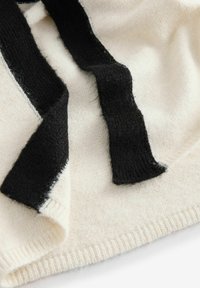 Knitted garment in cream wool with black wool ties. Textured, soft fabric with contrasting colors and a rolled hem detail.