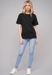 Schwarzes Baumwoll-T-Shirt mit kurzen Ärmeln und Rundhalsausschnitt, kombiniert mit hellblauen Skinny-Jeans und weißen Sneakers. Schlichtes, lässiges Outfit.
