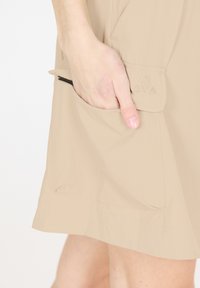 Beige rok van lichtgewicht stof met een zijzak. Heeft gestikte driehoekige details op de zakflap en een gladde textuur.