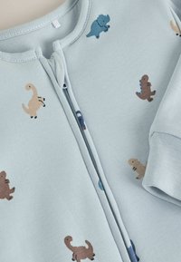 Hellblaues Reißverschluss-Overall aus weichem Stoff, mit kleinen, bunten Dinosaurier-Drucken. Rundhals und gerippte Bündchen.