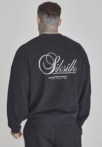 Felpa nera con un grande logo bianco "Siksilk" sulla schiena, accompagnata da un testo più piccolo di dettaglio. Realizzata in un morbido tessuto testurizzato.
