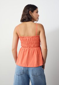 Coral peplum top with smocked bodice and thin checkered straps. Soft texture, lightweight fabric, and flared silhouette.